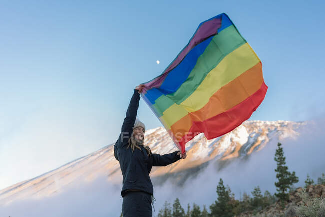 Pessoa em pico de montanha acenando com bandeira LGBT — Fotografia de Stock