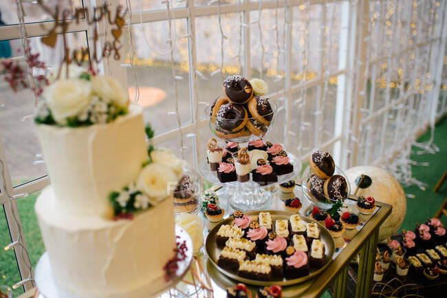 Зверху солодкі смачні вершкові шоколадні торти на круглому лотку з пончиками та ягідними тістечками на святковому столі в десертному барі в кафе — стокове фото