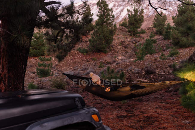 Warm gekleidete Frau in Hängematte am Baum im Scheinwerferlicht des Autos — Stockfoto