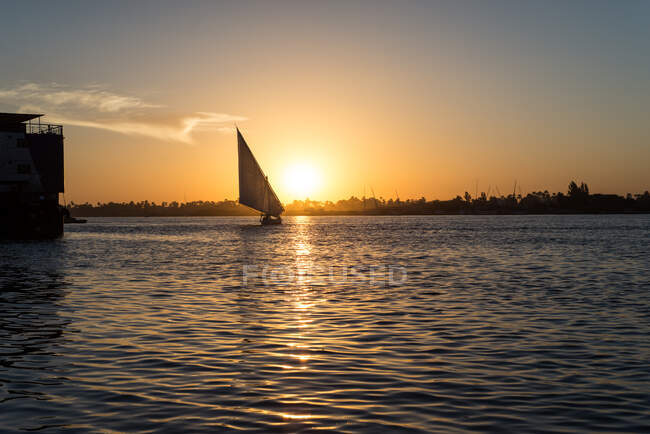 Paisaje pacífico de barco ligero maniobrable nadando en agua ondulada en la puesta del sol caliente, río Nilo, Egipto - foto de stock
