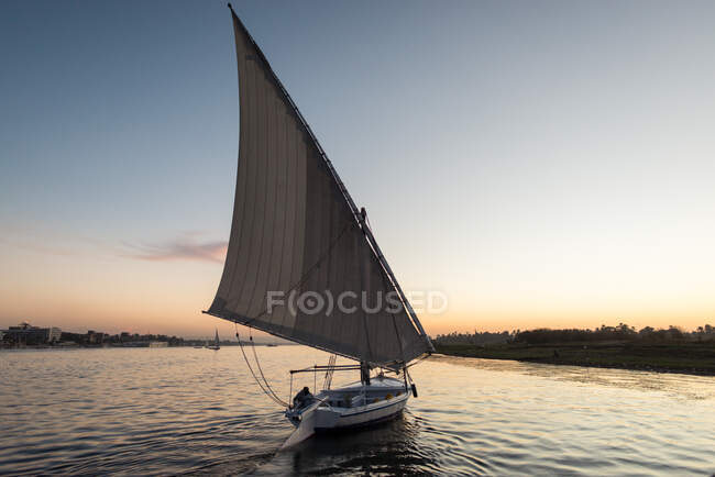 Paisaje pacífico de barco ligero maniobrable nadando en agua ondulada en la puesta del sol caliente, río Nilo, Egipto - foto de stock