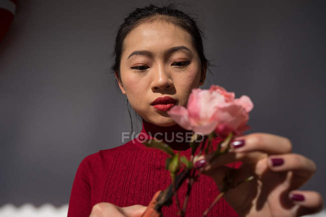 Young Asian woman cutting rose stem with secateurs — Stock Photo