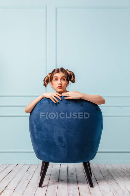 Chica adolescente posando detrás de un sillón azul sobre fondo turquesa - foto de stock