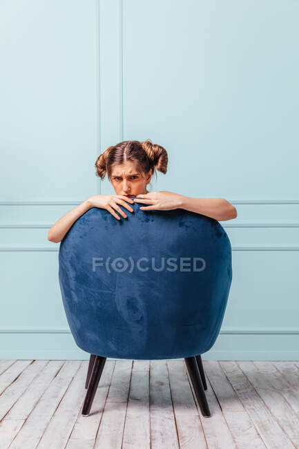 Adolescente enojada en un sillón azul sobre fondo turquesa - foto de stock