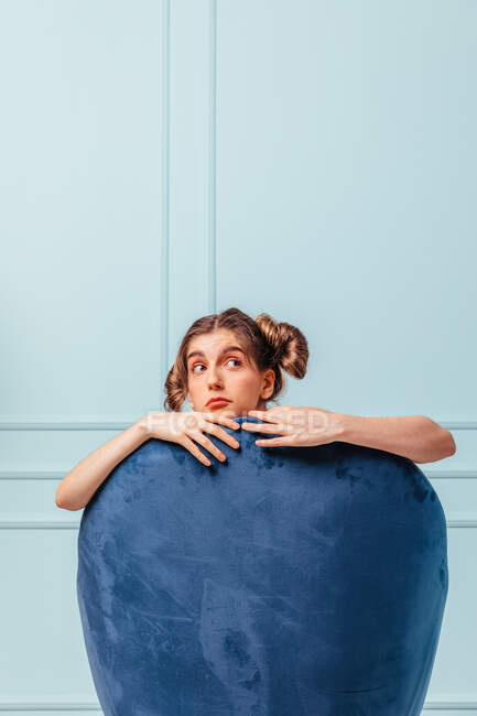 Испуганная девочка-подросток в синем кресле на бирюзовом фоне смотрит в сторону — стоковое фото