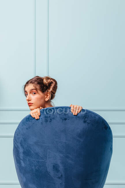 Teen girl posiert hinter einem blauen Sessel auf türkisfarbenem Hintergrund — Stockfoto