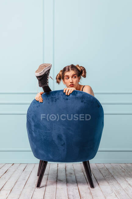 Adolescente chica oculta y feliz en un sillón azul sobre fondo turquesa - foto de stock