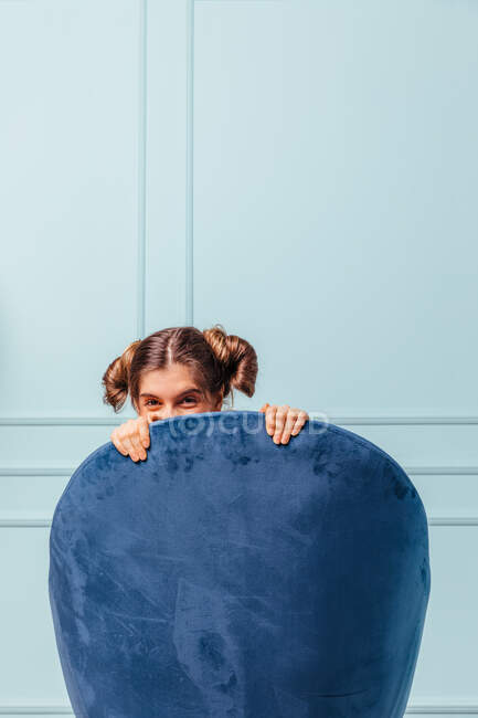 Menina adolescente escondida e feliz em uma poltrona azul no fundo turquesa — Fotografia de Stock