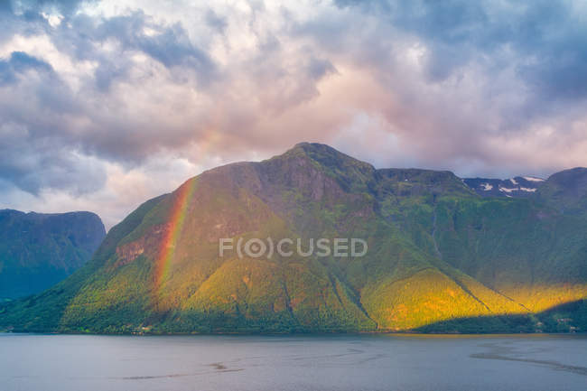 Misterioso paesaggio di arcobaleno colorato in montagne rocciose in acque calme sotto il cielo nuvoloso in Norvegia — Foto stock