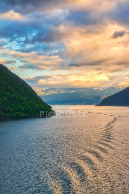 Gran paisaje increíble de la luz del sol a través del cielo nublado en el agua ondulada entre montañas rocosas en Noruega - foto de stock