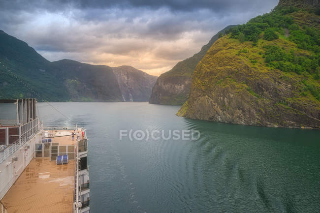 Big fast boat swimming in green water along mountains under cloudy sky in Norway — Stock Photo