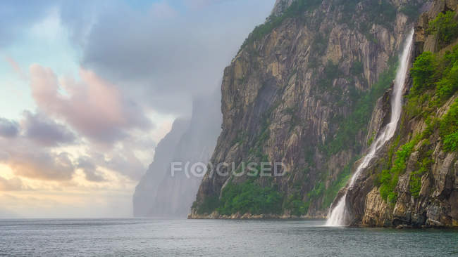 Fast speedy mountain river streaming down on rocky stony wall into calm water in Norway — Stock Photo