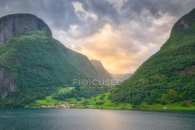 Impresionante paisaje en agua verde que refleja el cielo nublado lavando montañas rocosas con árboles verdes y hierba en Noruega - foto de stock