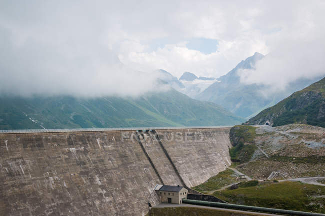 Haute route alpine sur grand barrage en arrière-plan avec des montagnes nuageuses et brumeuses en Autriche — Photo de stock