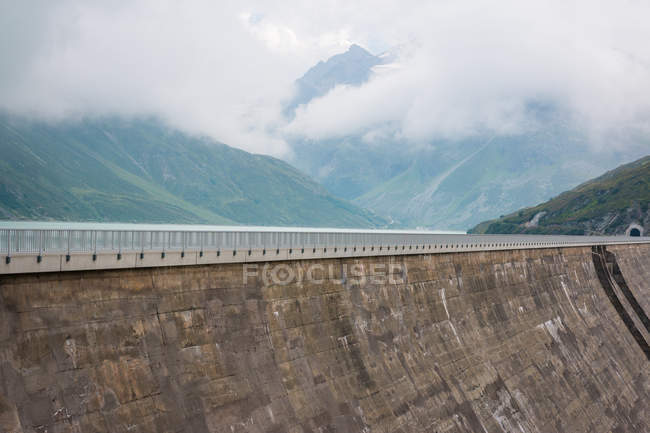High alpine road on big dam on background with misty cloudy mountains in Austria — Stock Photo