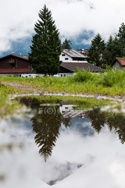 Calm transparent lake reflecting white cloudy sky and green tree on meadow in Austria — Stock Photo