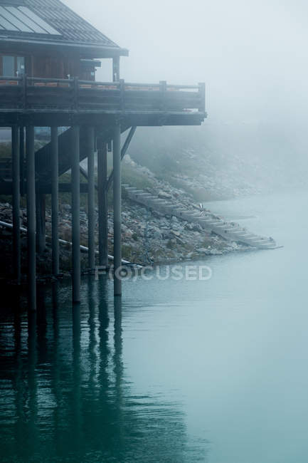 Misteriosa casa in legno sollevata su mucchi sopra la superficie del lago in tempo nebbioso in Austria — Foto stock