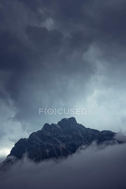 Dramático misterioso pico rocoso bajo nubes grises en niebla brumosa en Austria - foto de stock