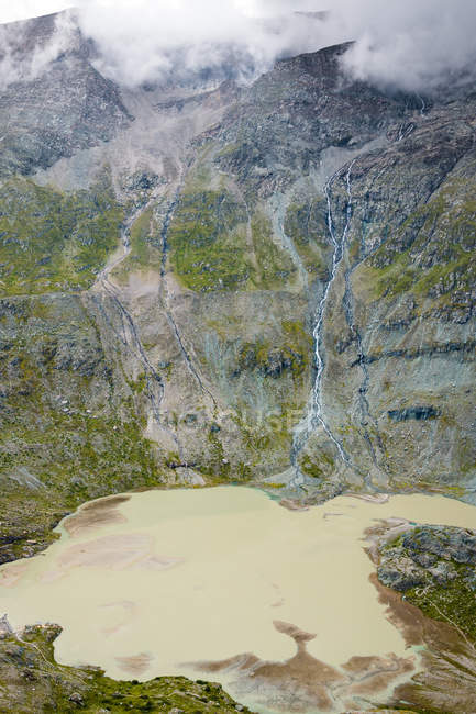 Lago con acqua fangosa situato vicino cresta di montagna grezza nella giornata nuvolosa in Austria — Foto stock