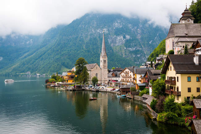 Чистый пруд с спокойной водой и прекрасные дома маленького городка, расположенного рядом с горным хребтом в пасмурный день в Австрии — стоковое фото