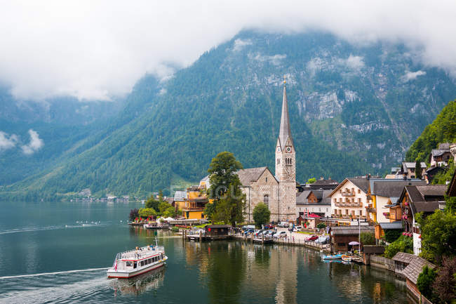 Чистый пруд с спокойной водой и прекрасные дома маленького городка, расположенного рядом с горным хребтом в пасмурный день в Австрии — стоковое фото