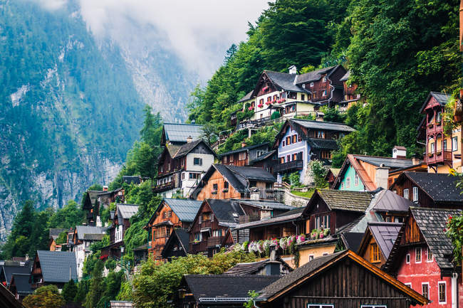 Уютные домики маленького поселка, расположенного рядом с лесом на горном склоне в облачный день в Австрии — стоковое фото