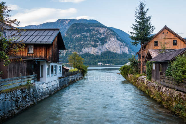 Kanal mit sauberem Wasser fließt an bewölkten Tagen durch ruhiges Dorf in bergigem Gelände in Österreich — Stockfoto