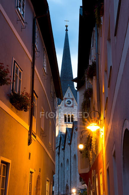 Снизу узкая улочка с яркими фонарями, расположенная возле церковной башни в тихом старом городке вечером в Австрии — стоковое фото