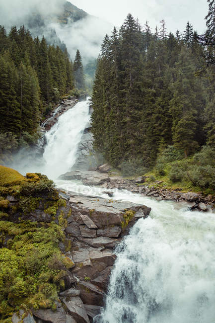 Sauberes Wasser fällt an einem nebligen Tag aus rauen Klippen in friedlicher Landschaft in Österreich — Stockfoto