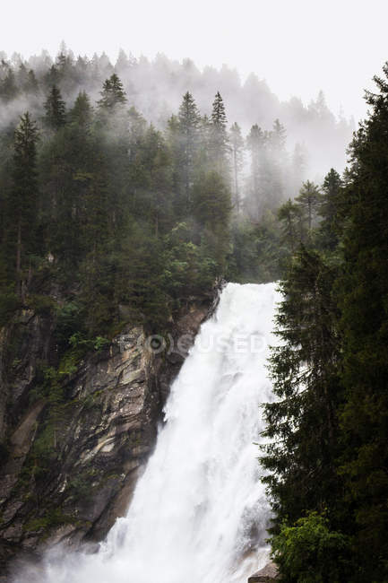 Sauberes Wasser fällt an einem nebligen Tag aus rauen Klippen in friedlicher Landschaft in Österreich — Stockfoto