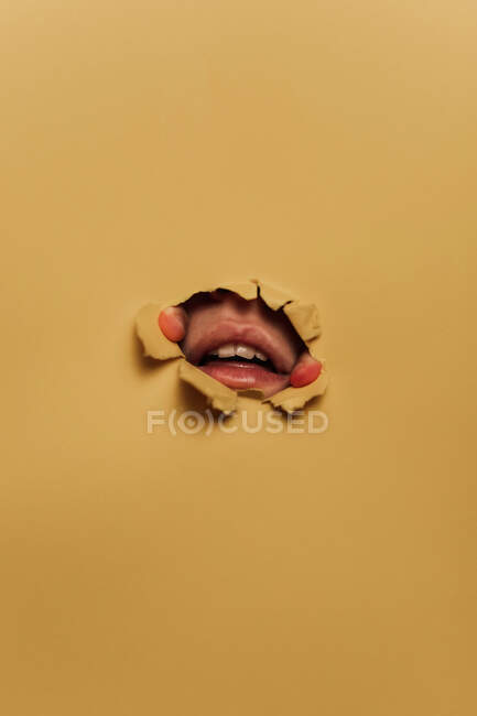 Persona irreconocible mostrando labios a través de un agujero de papel - foto de stock