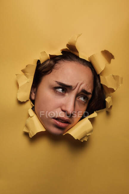 Thoughtful female teenager looking out from hole in studio — Stock Photo