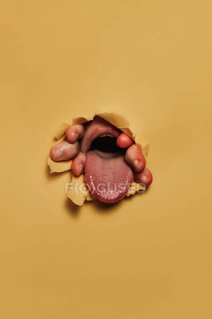 Pessoa irreconhecível mostrando a língua através do furo de papel — Fotografia de Stock