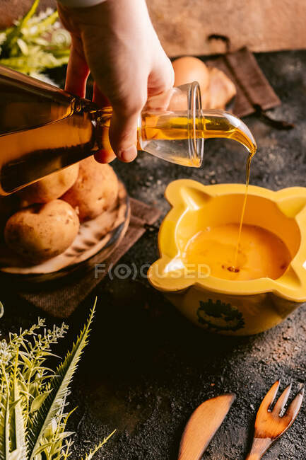 From above of crop woman pouring oil in bowl preparing for cooking dish in kitchen — Stock Photo