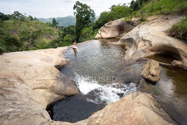 Mujer delgada nadando en piscina natural en cascada de montaña - foto de stock