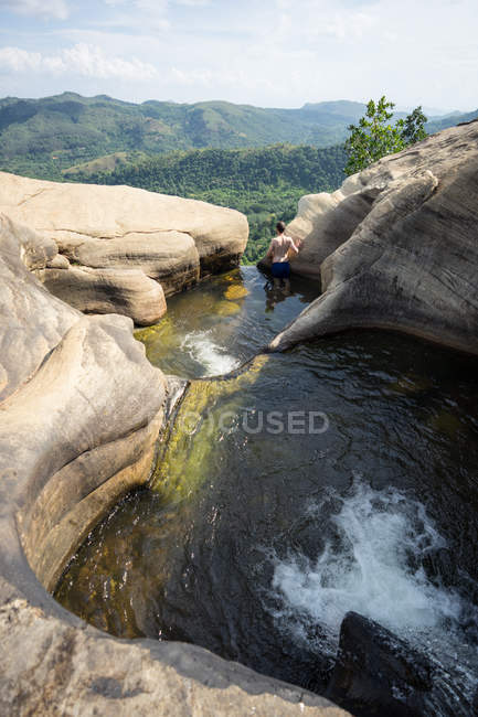 Hombre sorprendido disfrutando de las vistas y nadando en la piscina de piedra en la cascada de montaña - foto de stock