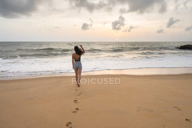 Back view of woman on vacation in casual wear enjoying view while walking at sandy empty seashore at Negombo beach — Stock Photo
