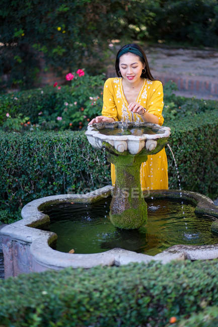 Happy asian woman smiling and touching clean fountain water while resting in garden of Alcazaba in Malaga, Spain — Stock Photo