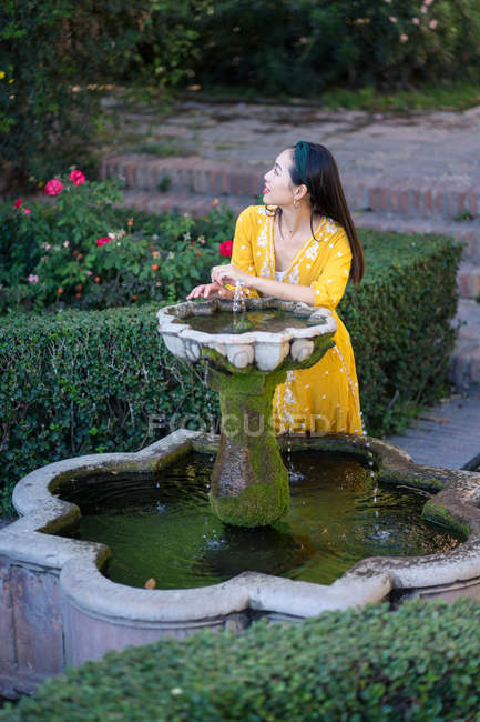 Asiatique femme toucher fontaine eau dans jardin — Photo de stock