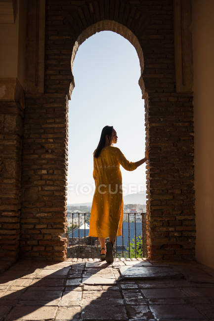 Rückansicht einer jungen Frau im Kleid, die im schäbigen Backsteinbogen von Alcazaba in Malaga, Spanien, steht und wegschaut — Stockfoto