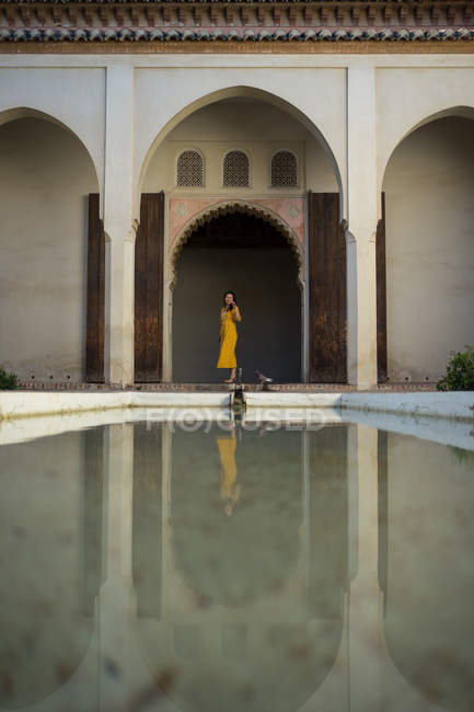Азиатка в жёлтом платье, стоящая в дуге возле спокойного бассейна во дворе Алькасабы в Малаге, Испания — стоковое фото