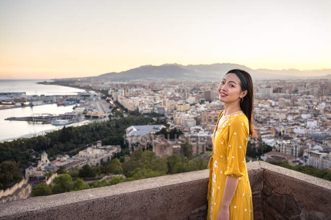 Feliz asiático turista contra ciudad y puesta de sol cielo - foto de stock