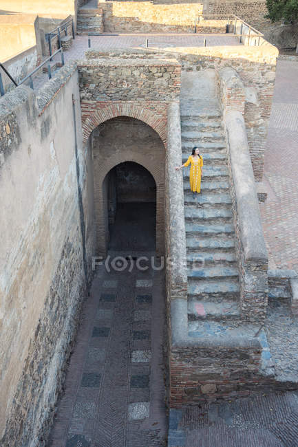 Von oben eine Frau in gelbem Kleid, die an einem sonnigen Tag in Málaga, Spanien, die alte Treppe des Castillo Gibralfaro hinuntergeht — Stockfoto