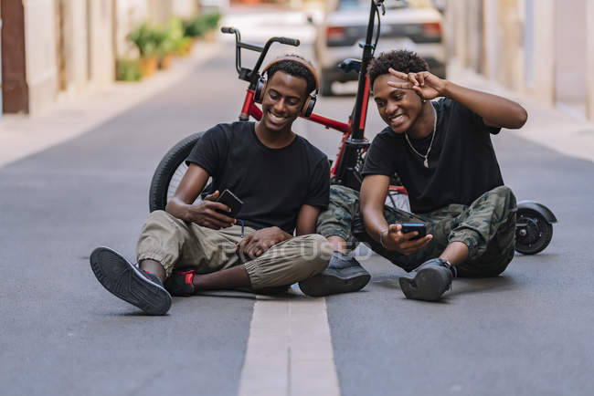 Cheerful youthful African American male teenager taking selfie pictures on cellphone with joyful black male friend in headphones — Stock Photo