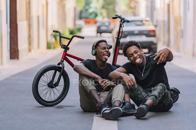 Jóvenes jovencitos y alegres adolescentes afroamericanos que toman fotos en el teléfono celular con un amigo masculino negro alegre en los auriculares. - foto de stock