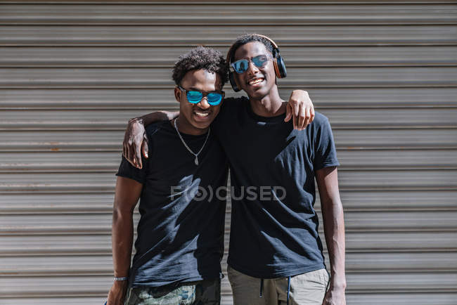 Happy youthful African American male teenagers in sunglasses enjoying pastime together while standing in sunlight in street — Stock Photo