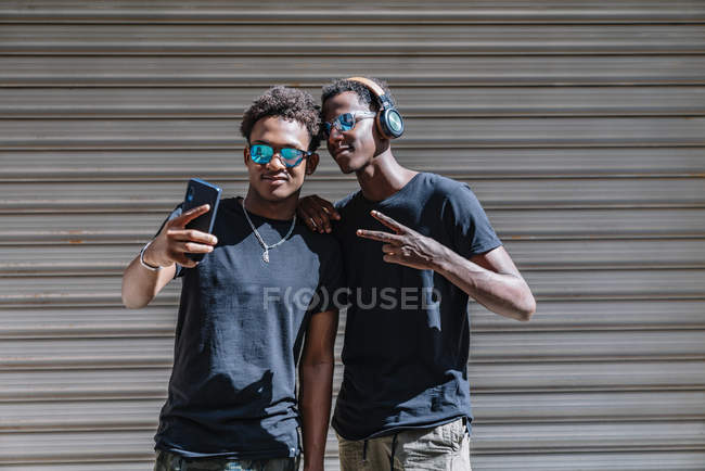 Jeune Américain d'origine africaine portant des lunettes de soleil prenant des photos avec son téléphone portable alors qu'il est au soleil dans la rue — Photo de stock
