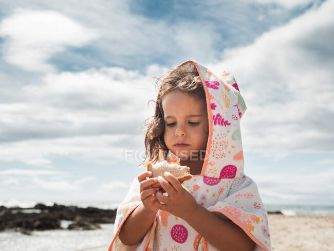 Little girl eating bread on beach — Stock Photo