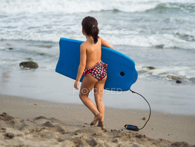 Chica irreconocible con tabla de natación en la playa - foto de stock