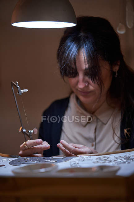 Beautiful artisan jeweler woman working in a jewelry shop with tools and a light bulb — Stock Photo